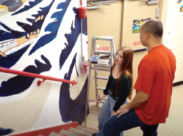 student and teacher painting a walll